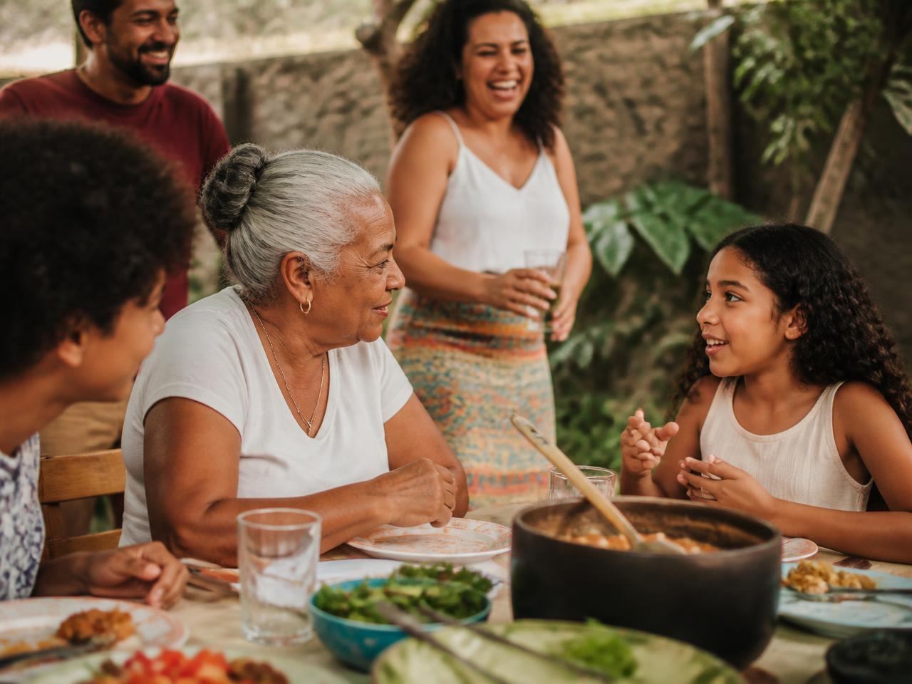 Família reunida à mesa em um almoço, avó conversando com a neta
